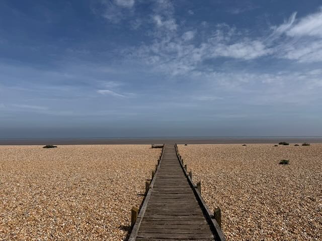 The wooden boardwalk at Greatstone leading out across the shingle to a calm sea